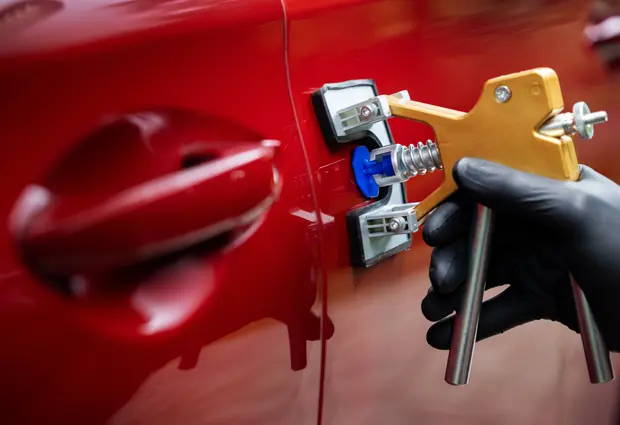 Glue-pulling tool attached to a red car door for paintless dent removal