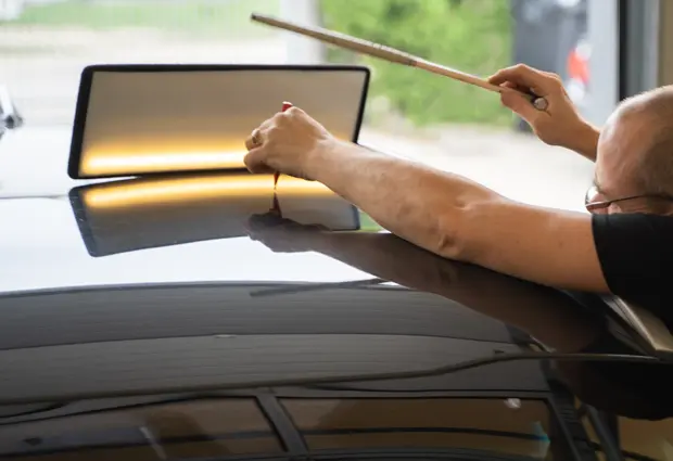 Technician using a tap-down tool and inspection light to repair dents on a car roof